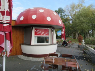 Fliegenpilz Mardorf Ein kleines Café in Mardorf mit fliegenpilzförmigem Dach, umgeben von einladenden Sitzgelegenheiten.