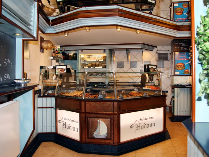 Fischerei & Aalräucherei Hodann GmbH Innenansicht der Aalräucherei mit gläserner Verkaufstheke, präsentiert verschiedene Fischprodukte.