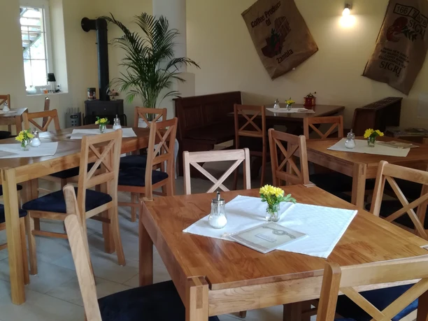 Light-flooded room with wooden chairs and tables, white tablecloths and yellow flower arrangements.