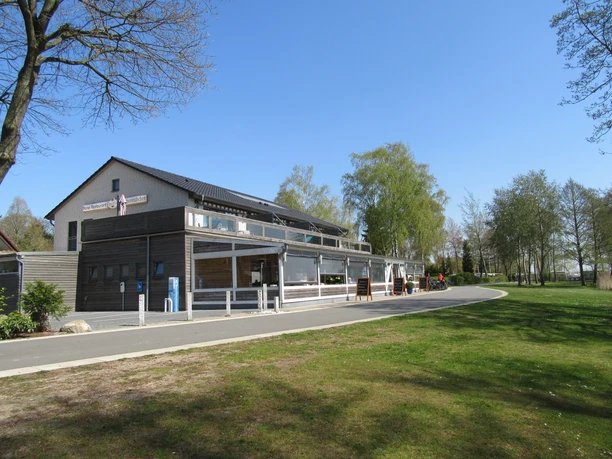 Fischerstübchen Ein modernes Restaurant mit großen Glasfronten, umgeben von Bäumen und angrenzend an eine ruhige Straße.