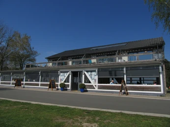 Fischerstübchen Ein zweistöckiges Restaurant mit großen Fenstern und überdachter Terrasse unter strahlend blauem Himmel.
