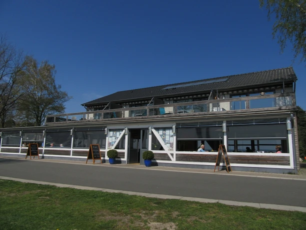 Fischerstübchen Ein zweistöckiges Restaurant mit großen Fenstern und überdachter Terrasse unter strahlend blauem Himmel.