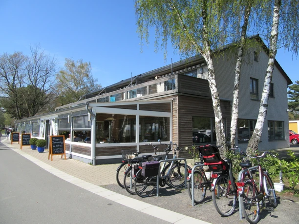 Fischerstübchen Ein modernes Restaurant mit Außenterrasse, umgeben von Bäumen und mit mehreren Fahrrädern davor geparkt.