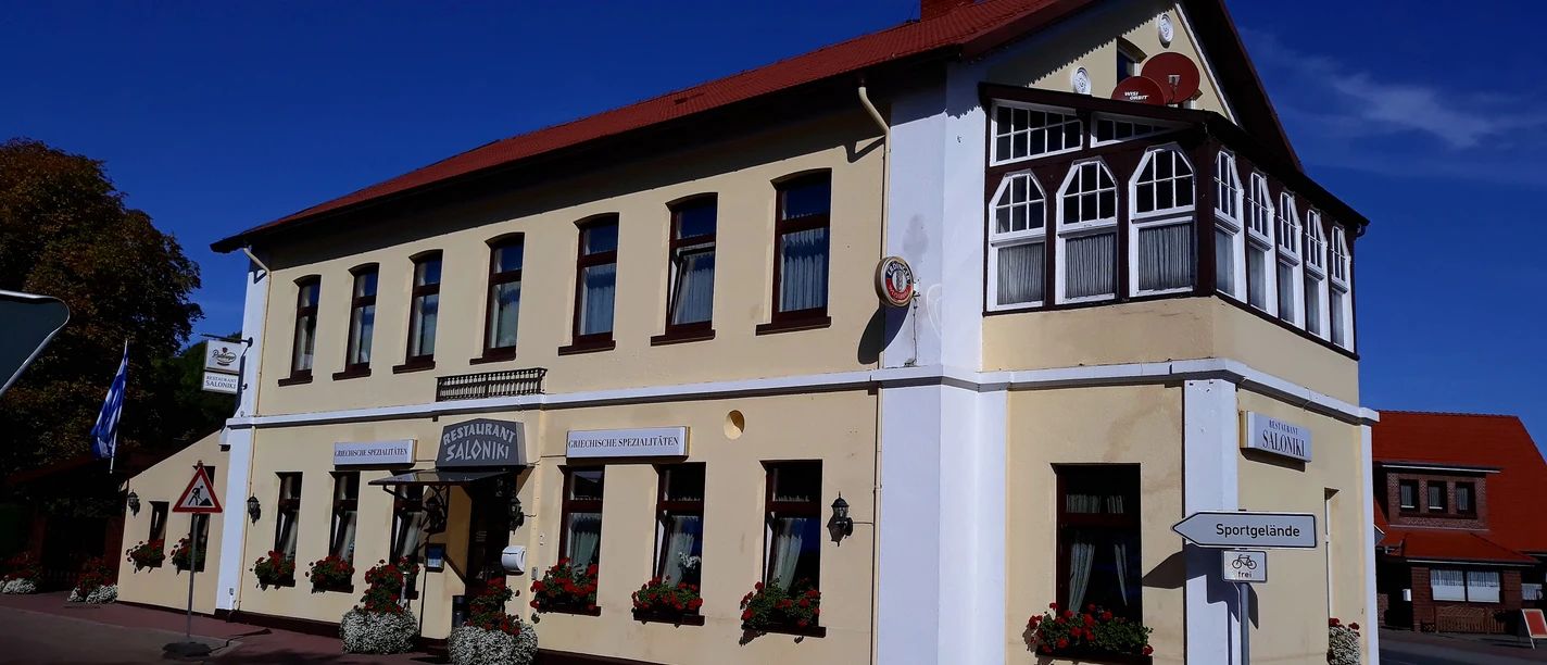 Restaurant Saloniki Das Restaurant Saloniki zeigt ein zweistöckiges Gebäude im traditionellen Stil mit weißen Wänden und roten Dachziegeln.