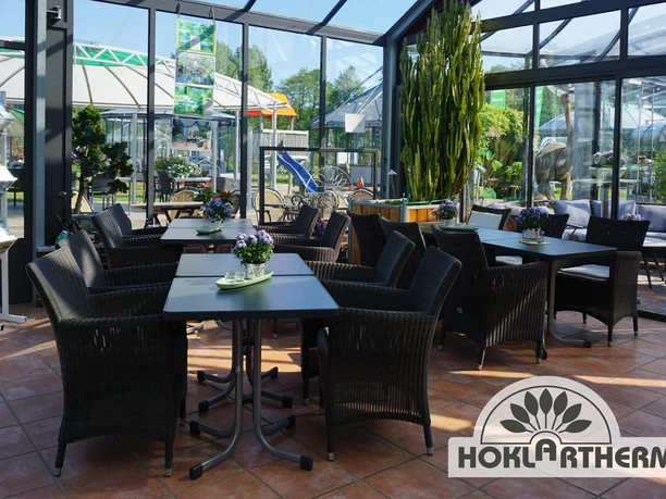 Orangerie Innenansicht Innenansicht einer lichtdurchfluteten Orangerie mit eleganten dunklen Rattanmöbeln auf Terrakottafliesen.