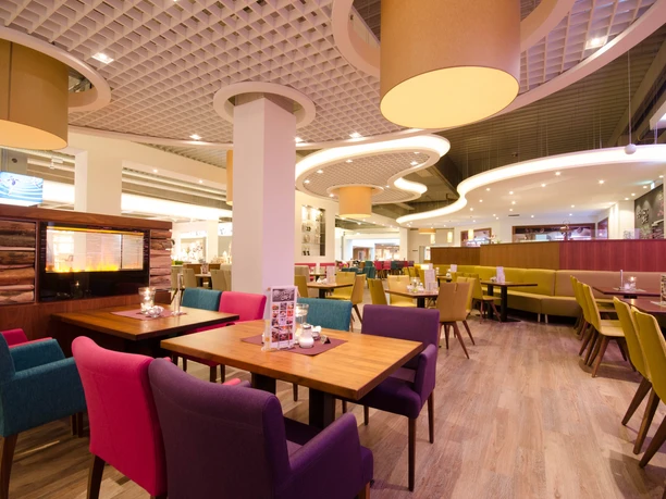 A tastefully furnished café with bright wooden tables, colorful upholstered chairs and warm lighting conjures up an inviting atmosphere.