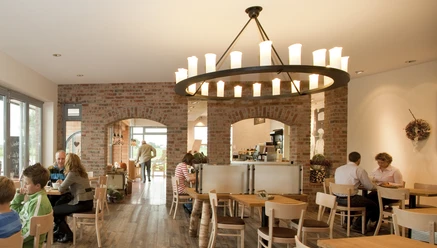 Bäckerei Ripken Innenansicht Inviting café with brick walls, wooden furniture and a large, rustic candle-look chandelier. Guests enjoy the ambience with coffee and pastries.