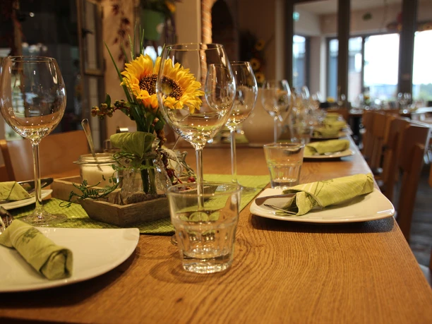 Bäckerei Ripken Rustikales Café-Ambiente mit gedecktem, hölzernem Tisch, grünen Servietten und frischen Sonnenblumen.