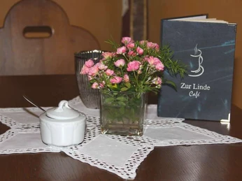 Gedeckter Tisch im Café zur Linde Ein gedeckter Holztisch im Café zur Linde mit Blumen, Zuckerdose und Menükarte auf weißem Deckchen.