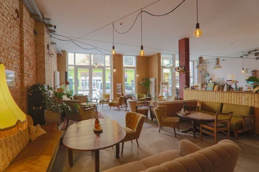 Heller Gastraum des Cafés Findus mit verschiedenen Vintage-Sitzmöbeln und Backsteinwand.