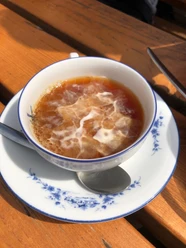 Teetied_waddensea.travel_ostfriesland.jpg Ostfriesentee mit einem Sahnewölkchen in einer weiß-blauen Tasse auf einem Holztisch.