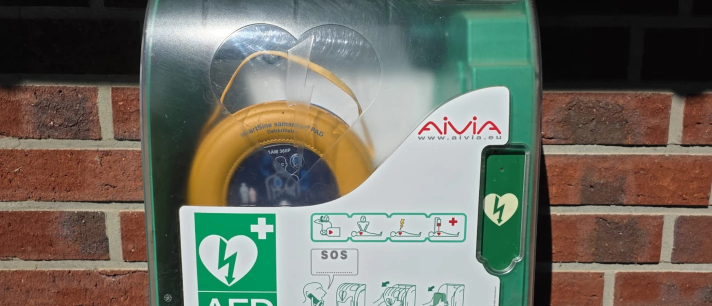 Defibrillator Wohnmobilstellplatz Steinhude Der Defibrillator am Wohnmobilstellplatz in Steinhude. Das orangene Gerät hängt in einem grünen Kasten vor einer Ziegelsteinwand.
