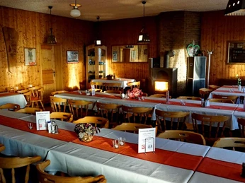 Ein rustikaler Gastraum mit Holzmobiliar und dekorativem Kamin, geschmückt mit roten Tischläufern.