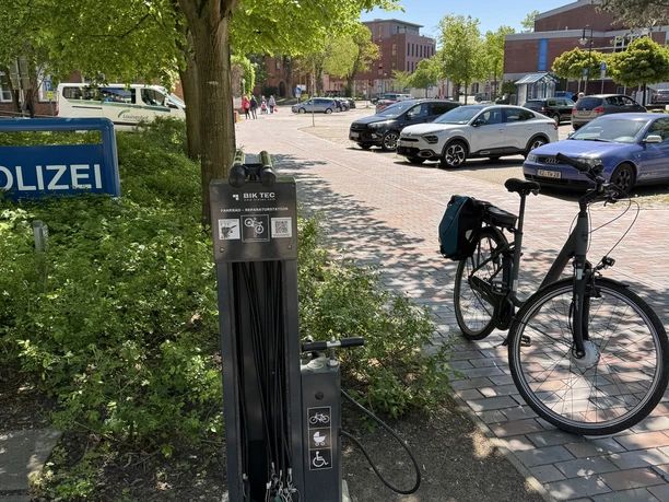 Radservicestation Schwarzenbek (Polizei) Outdoor bike repair station by a police sign with parked cars and a bike in sunlight