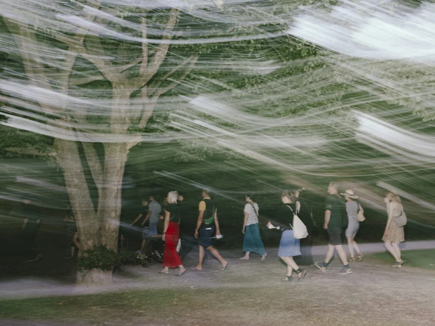 ritual: Musik, Spaziergänge und Community Menschen gehen im Park unter Bäumen, umgeben von starken Licht- und Bewegungsstreifen.