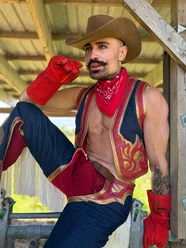 Tinus Eine Person im Cowboykostüm in Rot und Gold mit Hut, Bandana und Handschuhen, posierend in Holzrahmen