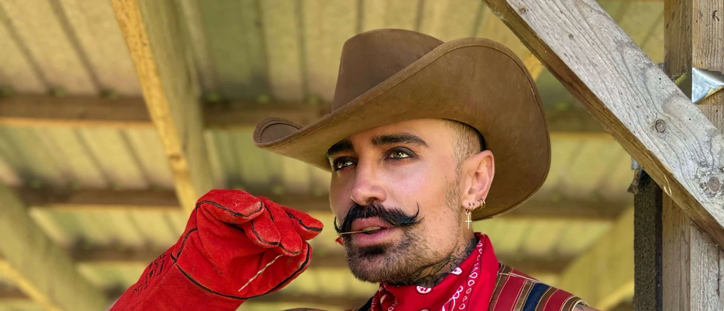 Tinus A person in a cowboy costume in red and gold with hat, bandana and gloves, posing in a wooden frame