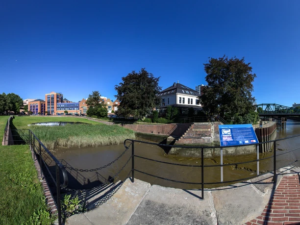 VomUrsprungderStadt_Wencke Dock(c)Helmut_Gross_WEB.jpg Historisches Wencke-Dock in Bremerhaven bei Sonnenschein, umgeben von Wasser, Bäumen und Häusern.