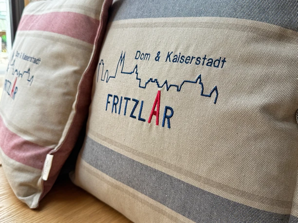 Fritzlar Tourist-Info_20250417_01 (MR) 4zu3 StadtmarketingFritzlar_CC-BY-SA.png Auf dem Foto sehen Sie zwei Kissen mit gestickter Silhouette von Fritzlar