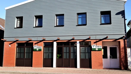 Brasserie Piano Fassade der Brasserie Piano mit rotem Backstein, grauer Holzverkleidung und dunklen Fenstern.
