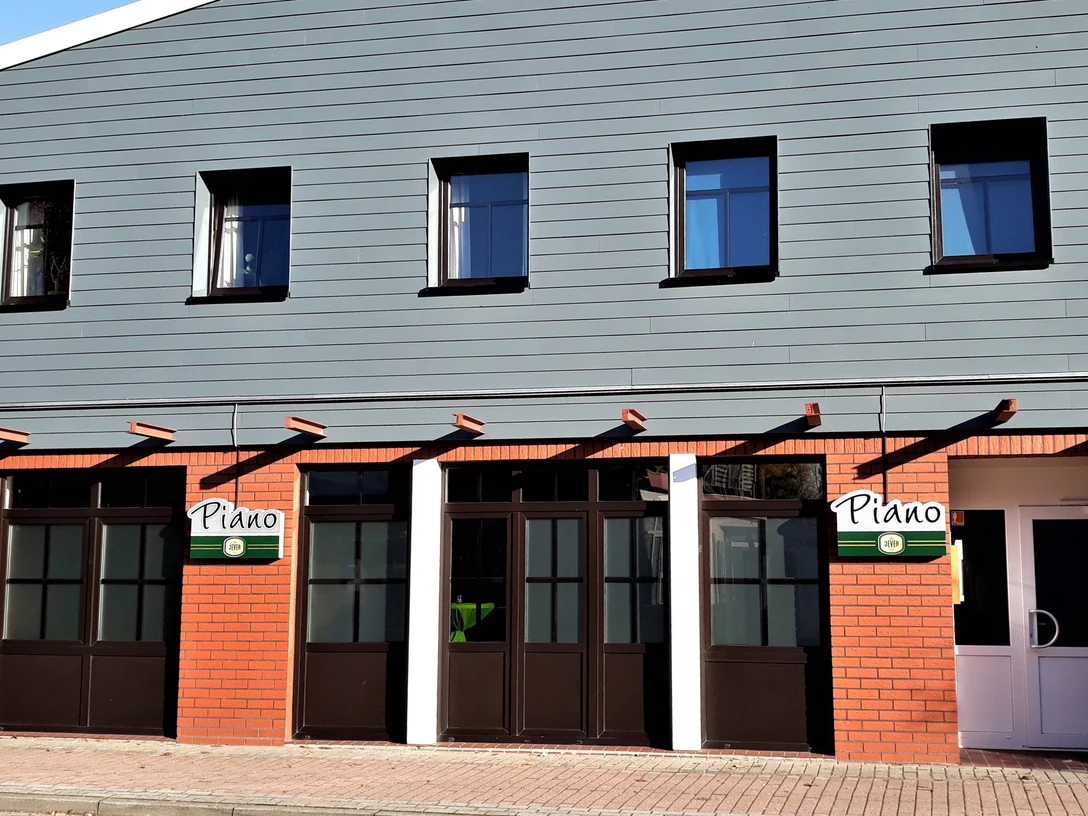 Brasserie Piano Fassade der Brasserie Piano mit rotem Backstein, grauer Holzverkleidung und dunklen Fenstern.