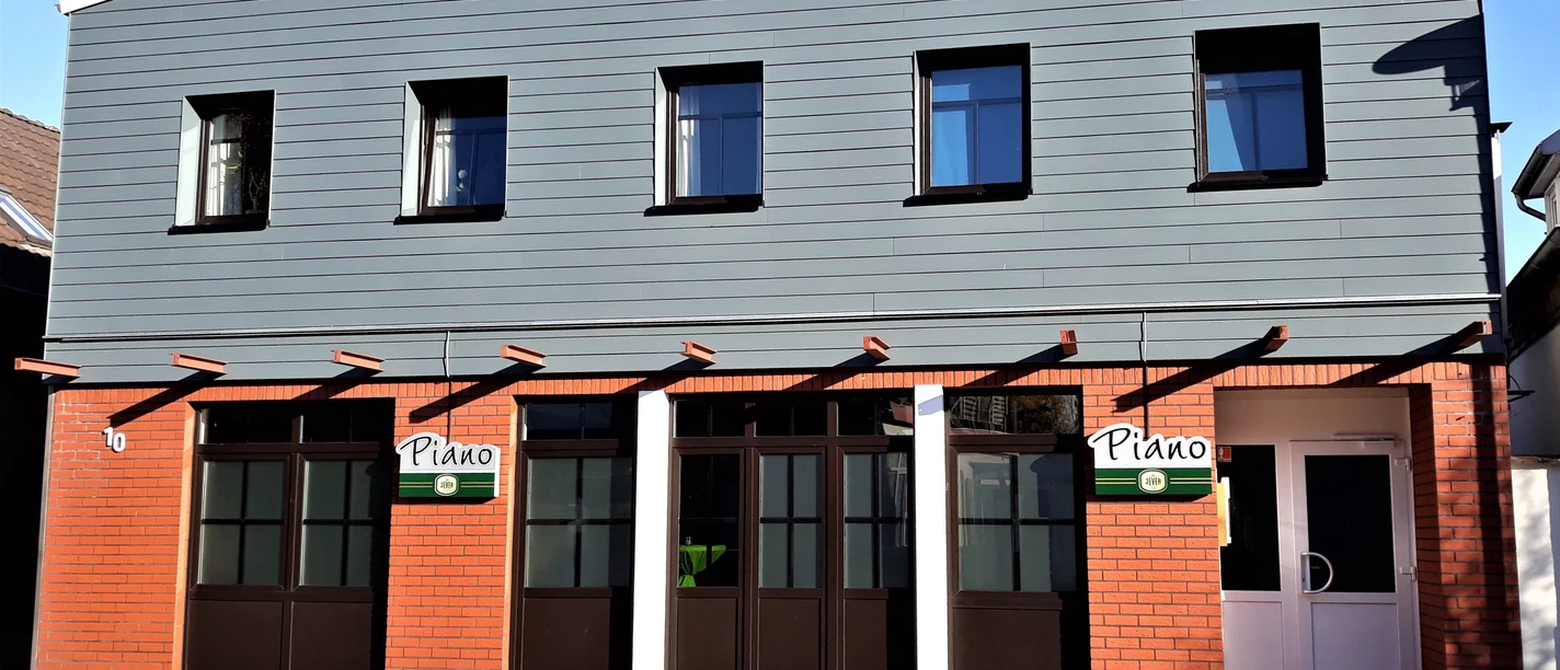 Brasserie Piano Fassade der Brasserie Piano mit rotem Backstein, grauer Holzverkleidung und dunklen Fenstern.