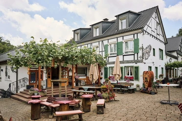 Biergarten im Restaurant Kleine Schweiz in Velbert Biergarten des Restaurants Kleine Schweiz in Velbert mit Holztischen unter Bäumen vor Fachwerkkulisse.