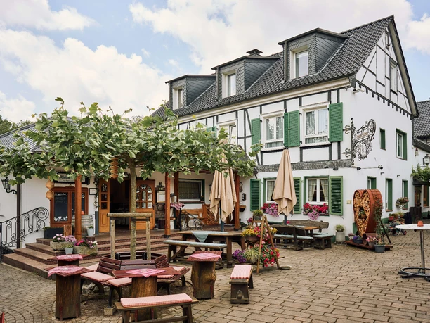 Biergarten im Restaurant Kleine Schweiz in Velbert Biergarten des Restaurants Kleine Schweiz in Velbert mit Holztischen unter Bäumen vor Fachwerkkulisse.