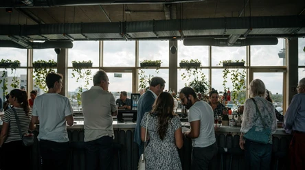 Monkey Bar indoor area People stand at a bar in front of large windows with plants and a room flooded with light.