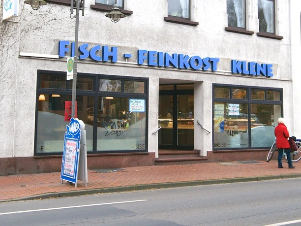 gastro-meppen-klene Straßenansicht eines Fisch-Imbisses mit blauer Beschriftung und einer Person mit roter Jacke vor dem Eingang.