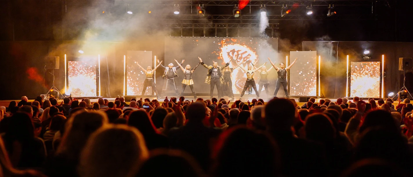 2026-LE_DIE_AGENTUR-177.jpg Darsteller in aufwändigen Kostümen beim Finale einer Musical-Show vor einem großen Publikum.