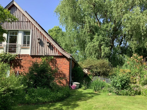 FeWo Lustiger Strump Backsteinhaus mit Holzgiebel und einem großen, grünen Garten mit altem Baumbestand bei Sonnenschein.