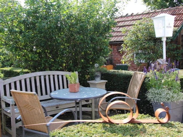Garten Ein gepflegter Garten mit einer gemütlichen Holzbank, einem runden Tisch und einem Haus im Hintergrund.