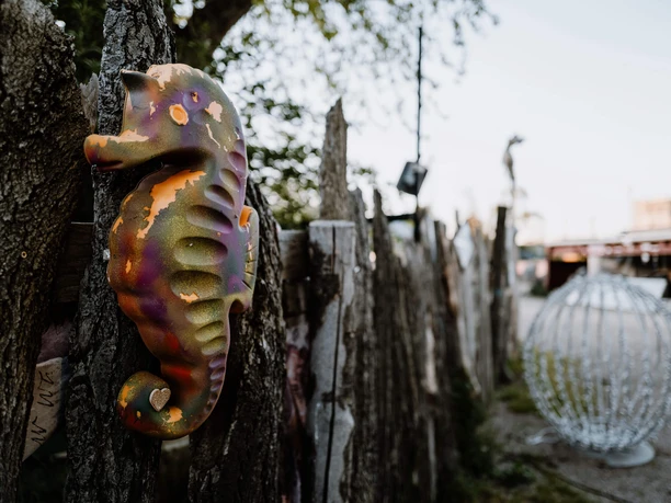 TAGTRAUM FESTIVAL Buntes Seepferdchen an Holzlatten, daneben steht eine metallene Kugelskulptur im Außenbereich