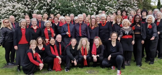 Rastede Gospel Choir.jpg Gruppenporträt des lächelnden Rastede Gospel Chors in Schwarz und Rot gekleidet in einem Garten.