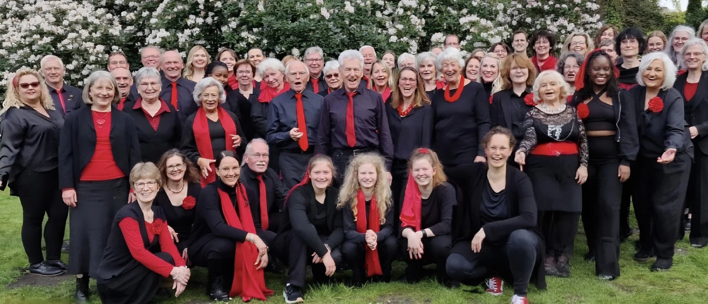 Rastede Gospel Choir.jpg Gruppenporträt des lächelnden Rastede Gospel Chors in Schwarz und Rot gekleidet in einem Garten.