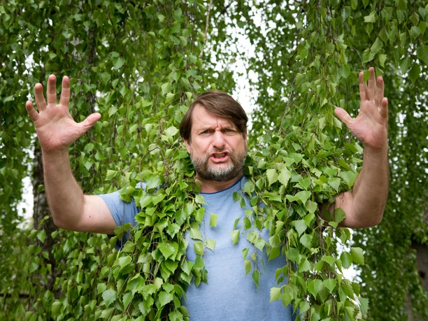 Peter Trabner Schauspieler mit erhobenen Händen, von Birkenzweigen umgeben, im Park