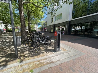 Fahrrad-Reparaturstation Warrington Platz 10 Fahrrad-Reparaturstation in Hilden mit parkenden Fahrrädern unter Bäumen auf einem gepflasterten Platz.