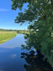 Die Ems Flusslauf zwischen Wiesen und Bäumen unter blauem Himmel in Gütersloh