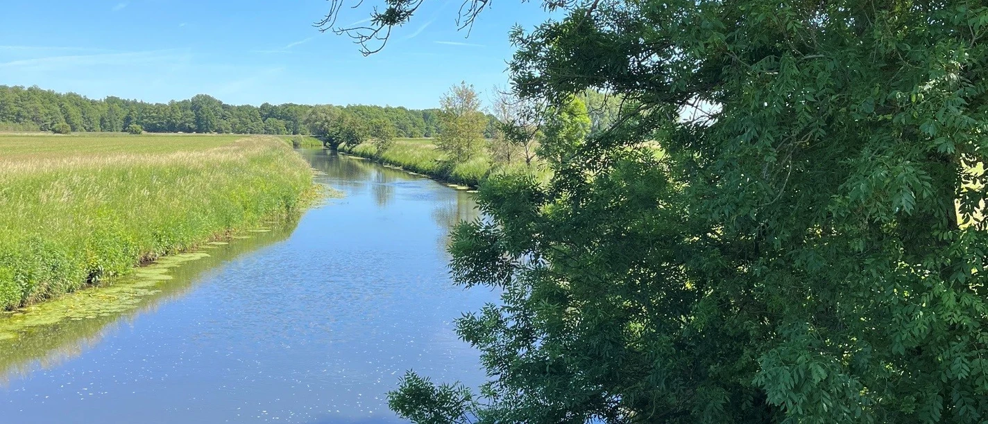 Die Ems Flusslauf zwischen Wiesen und Bäumen unter blauem Himmel in Gütersloh