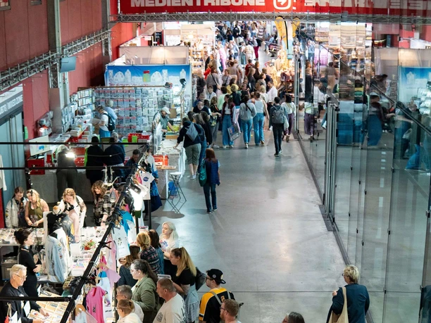 Kölner Creativ Sommer Besucher schlendern durch eine Messehalle mit bunten Ständen und vielfältigem Kreativangebot.