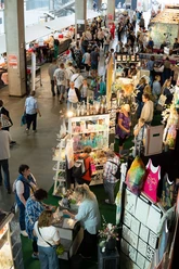 Kölner Creativ Sommer Menschen schlendern durch eine Messehalle mit dicht gereihten Kreativständen und vielfältigen Produkten.