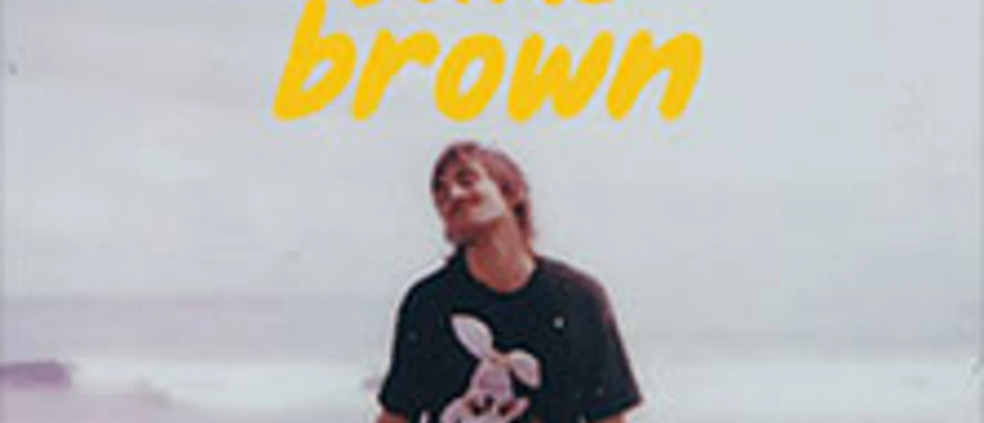 Person am Strand mit dunklem Shirt und gelber Schrift martin luke brown darüber