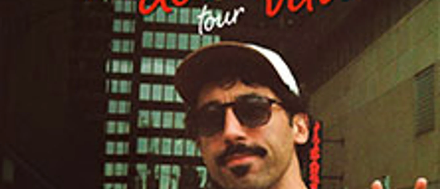Mann mit Sonnenbrille zeigt Peace-Zeichen vor hohen Gebäuden, Tourtitel im Bild.