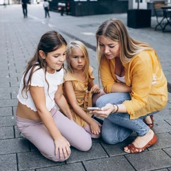 Kiddy Trip - The digital city rally for the family Woman with two children looking at a smartphone on a paved street.