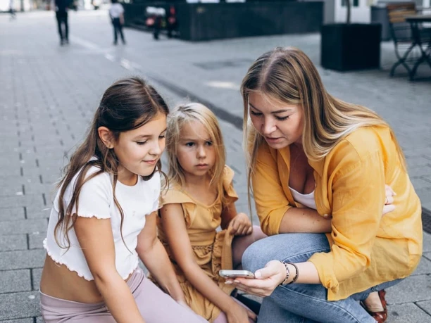 Kiddy Trip - The digital city rally for the family Woman with two children looking at a smartphone on a paved street.