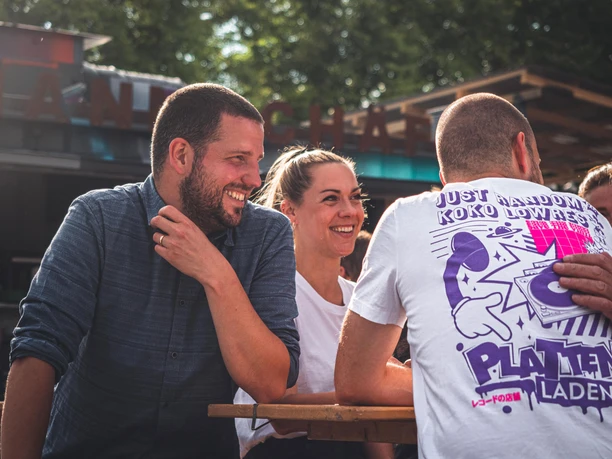 Johann Schäfer beer garden on the Rhine in Rheinauhafen Group of people laughing together at a wooden table in the open beer garden in the sunlight