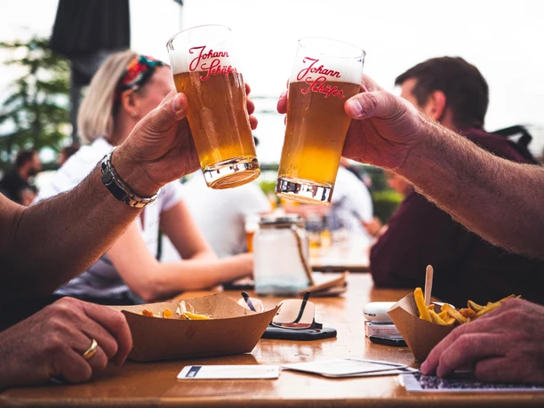 Johann Schäfer beer garden on the Rhine in Rheinauhafen Two hands clink bright beer glasses over a table of chips in the beer garden