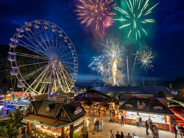 F1000-Fireworks4k.jpg Buntes Feuerwerk über dem Fest der 1000 Laternen, daneben ein leuchtendes Riesenrad und Buden.