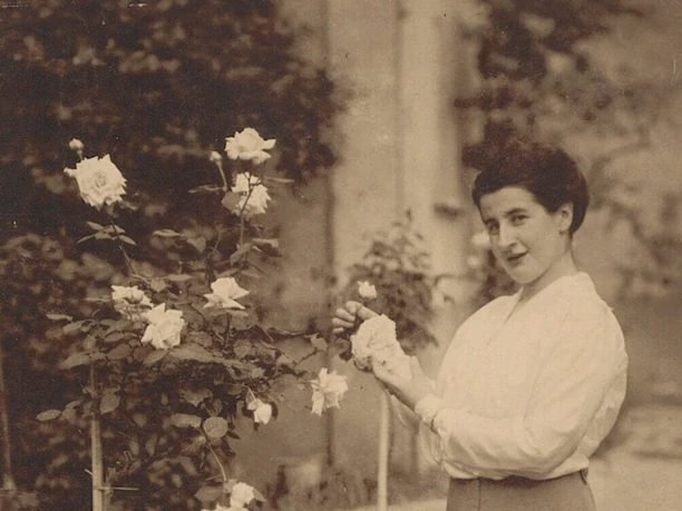 Olga Oppenheimer in the rose garden, around 1910 Woman in historical dress stands in the garden and looks at flowering rose bushes.